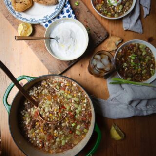 Stacy Lyn's vegetable beef soup in Dutch oven with ladle alongside bowls of soup on wooden table