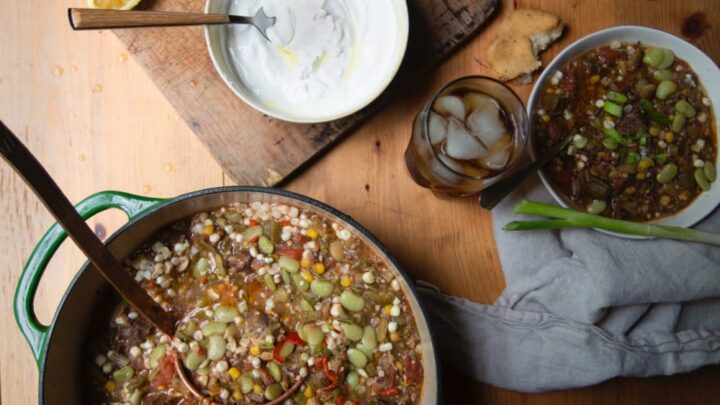Stacy Lyn's vegetable beef soup in Dutch oven with ladle alongside bowls of soup on wooden table