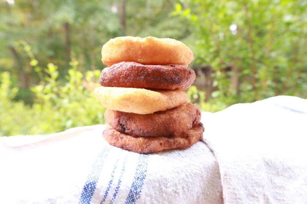 stack of golden fried corn patties - arepas - stacked on blue-striped white towel on porch railing