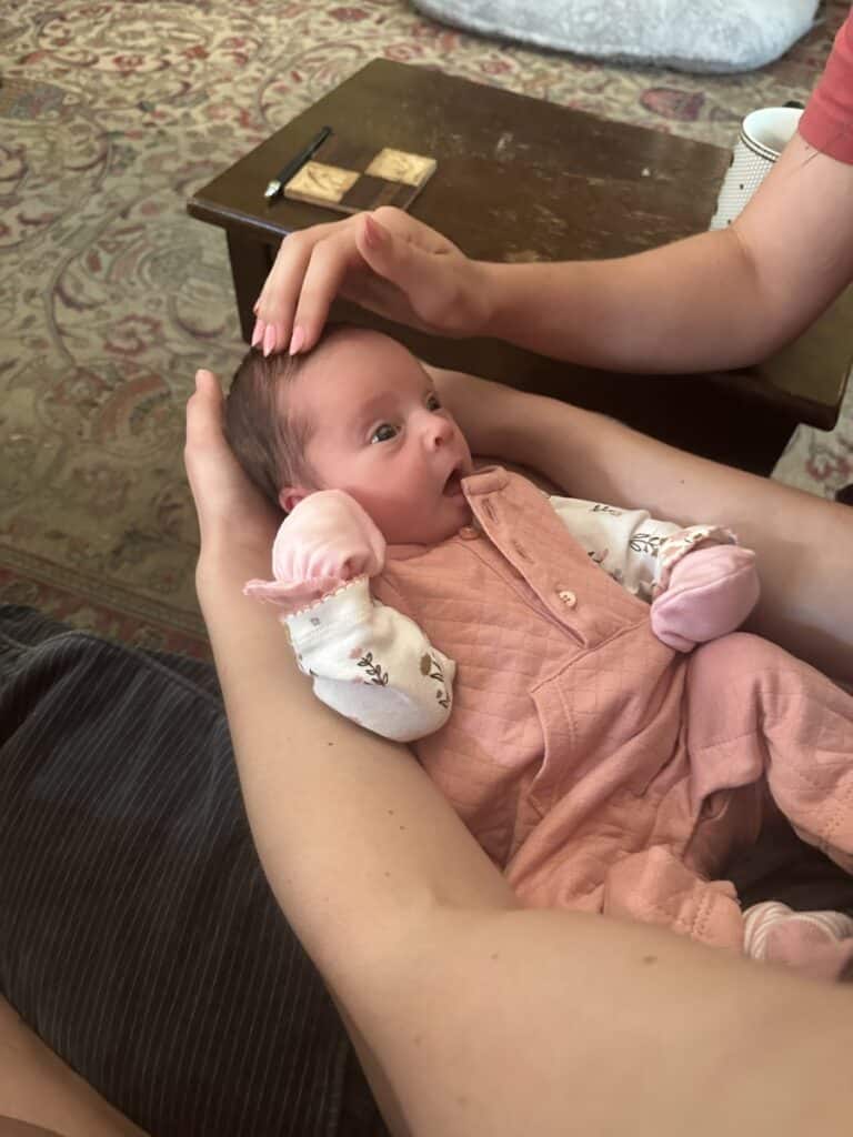 newborn baby Flora held in arms, wearing pink onesie