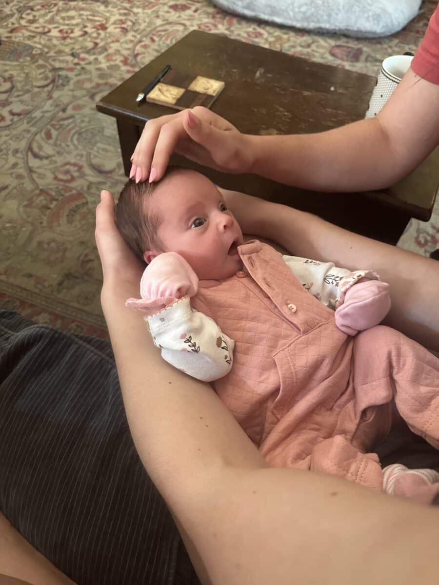 newborn baby Flora held in arms, wearing pink onesie