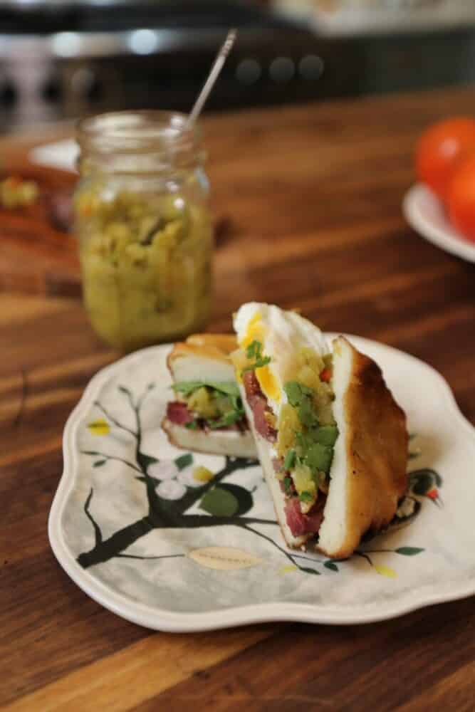 meat sandwich half on white plate with layer of green tomato relish from Stacy Lyn's recipe; jar of relish in background