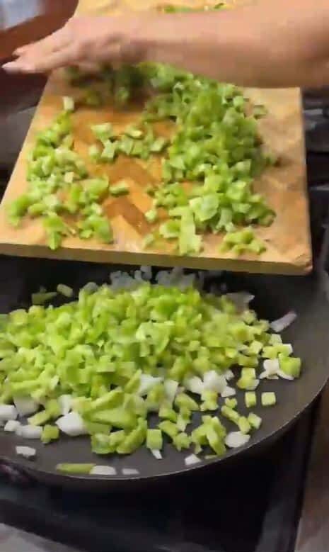 Stacy Lyn scraping chopped tomatoes and other vegetables from wooden cutting board into pan to cook