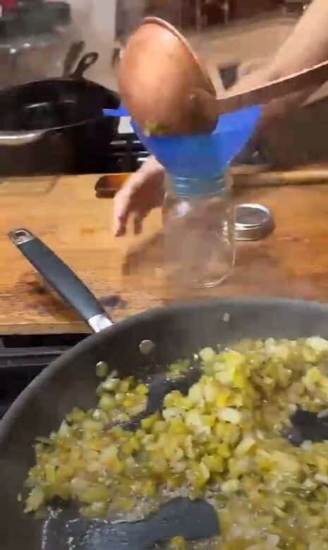 transferring cooked relish from pan into pint jars with a blue funnel