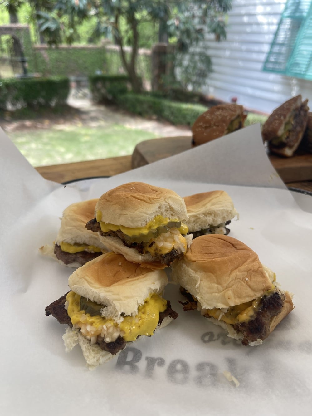 stack of venison copycat krystal burgers on white paper on plate in Stacy Lyn's backyard