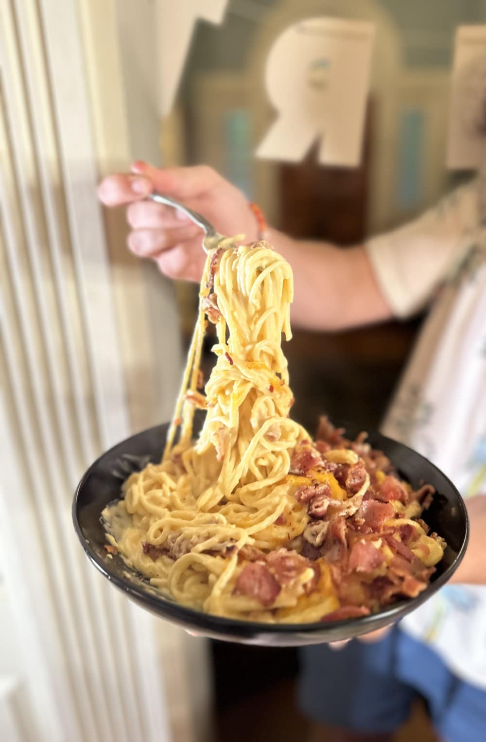 heaping plate of New Orleans mac and cheese spaghetti held by Stacy Lyn with fork twirling and lifting the spaghetti