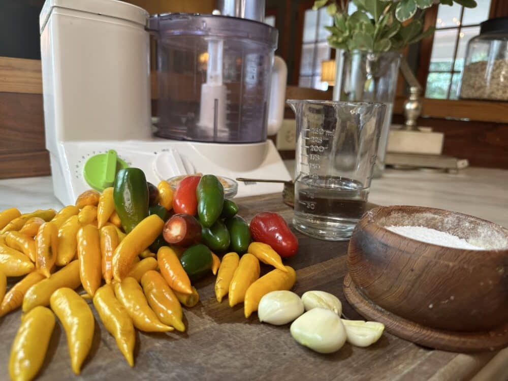 jalapenos and other hot peppers on counter with sriracha ingredients in front of blender / food processor