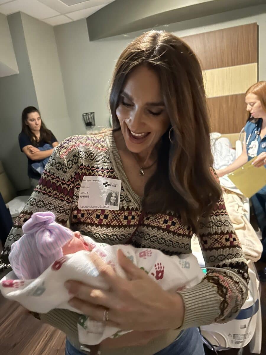 smiling Stacy Lyn holding newborn baby Flora in hospital room