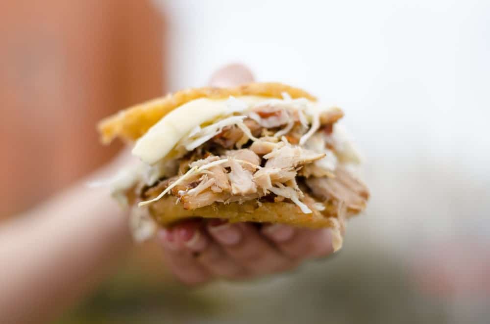 hand holding venezualan arepas sandwich stuffed with meat and cheese