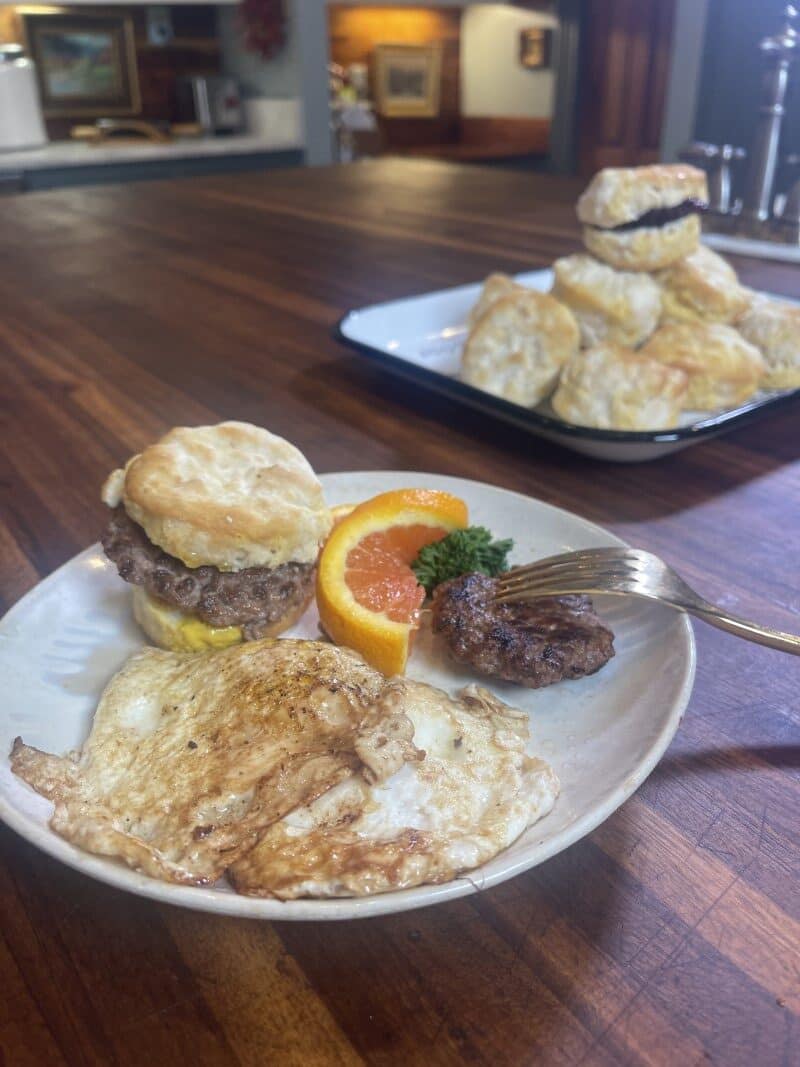 plate on counter with fried eggs and venison sausage breakfast bisuits - tray of more biscuits in background