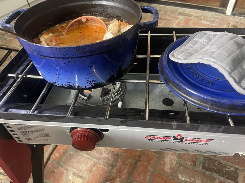 fish stew cooking in a blue enamel pot on an outdoor gas grill