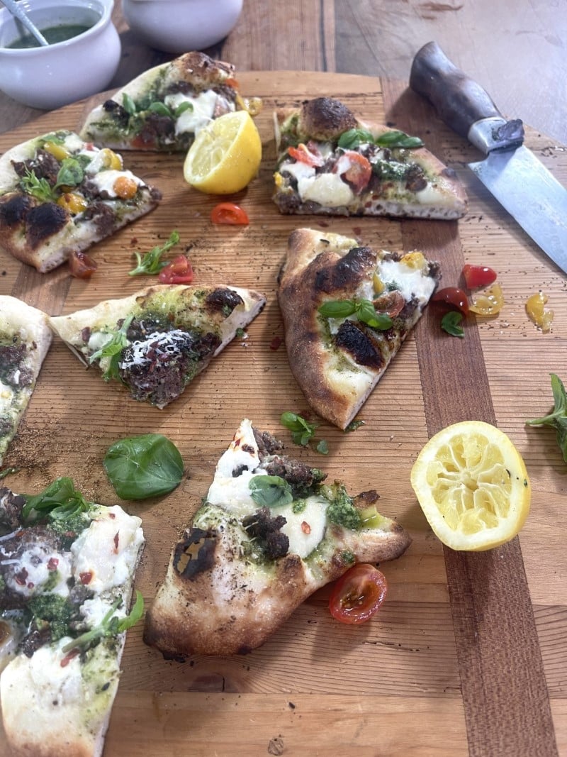 small slices of turkey pizza with burrata cheese and walnut pesto on cutting board with two lemon halves and grape tomato halves
