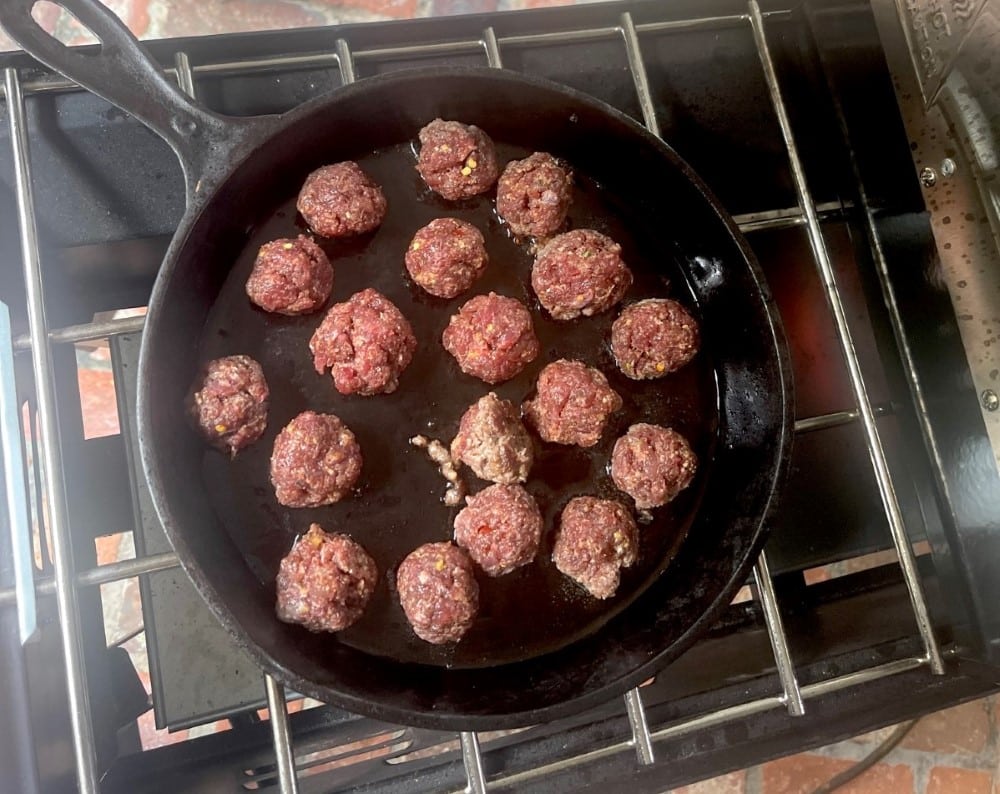 turkey sausage balls cooking in cast iron pan on grill