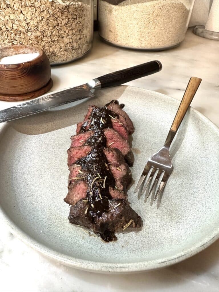 venison medallions with cabernet mushroom sauce on white plate with fork and knife