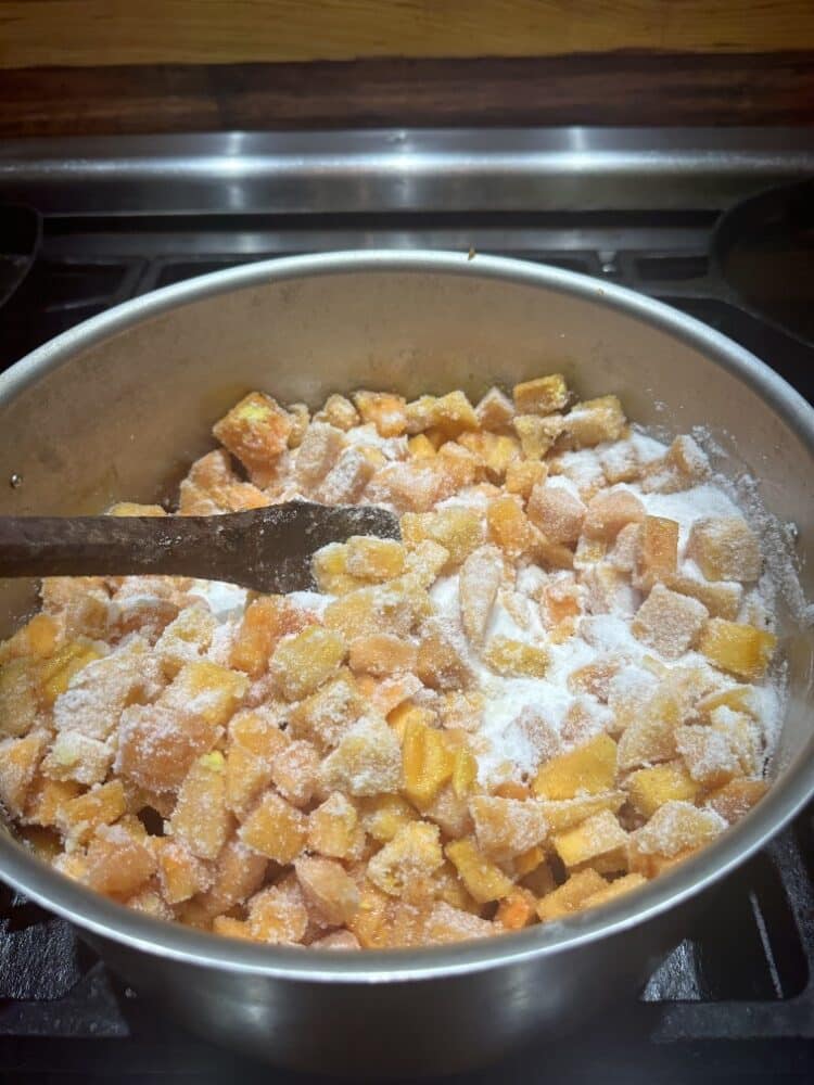 cubed persimmon fruit flesh cooking in large pot, stirred with wooden spoon