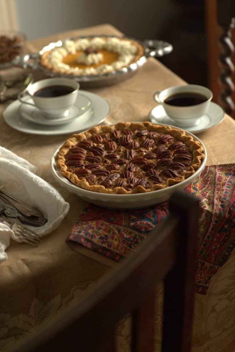 freshly baked Southern pecan pie on table with coffee cups and a pumpkin pie