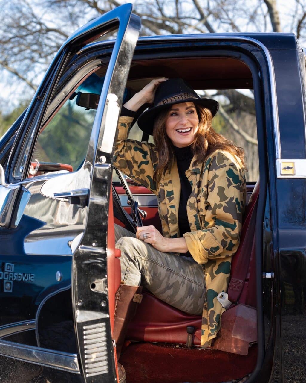 Stacy Lyn sitting in truck with open door, smiling in camo and hat