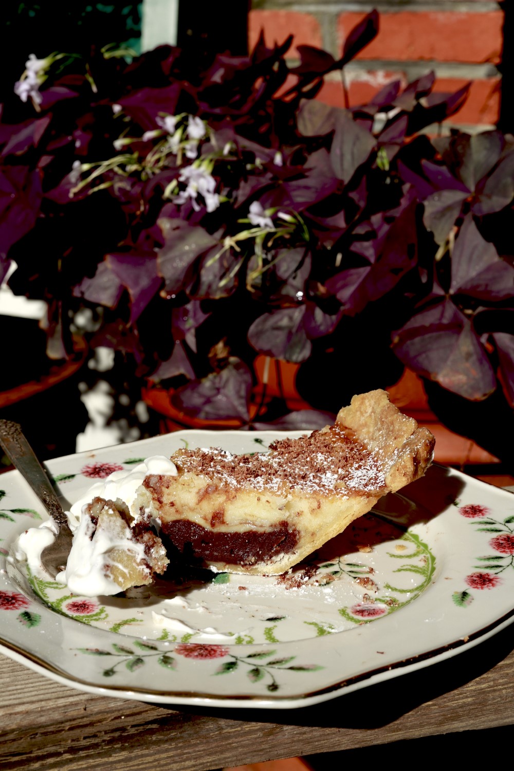 slice of black bottom buttermilk pie with vanilla ice cream on floral plate with dark red blooming plant in background