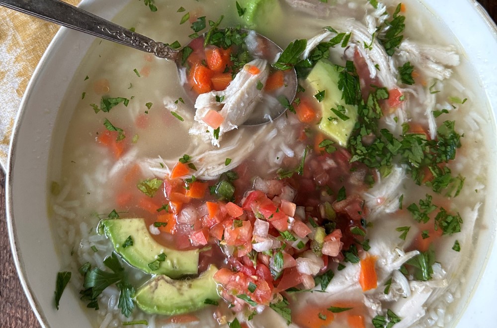 closeup of homemade Mexican chicken soup with avocado and pico de gallo in white bowl with spoon in the soup