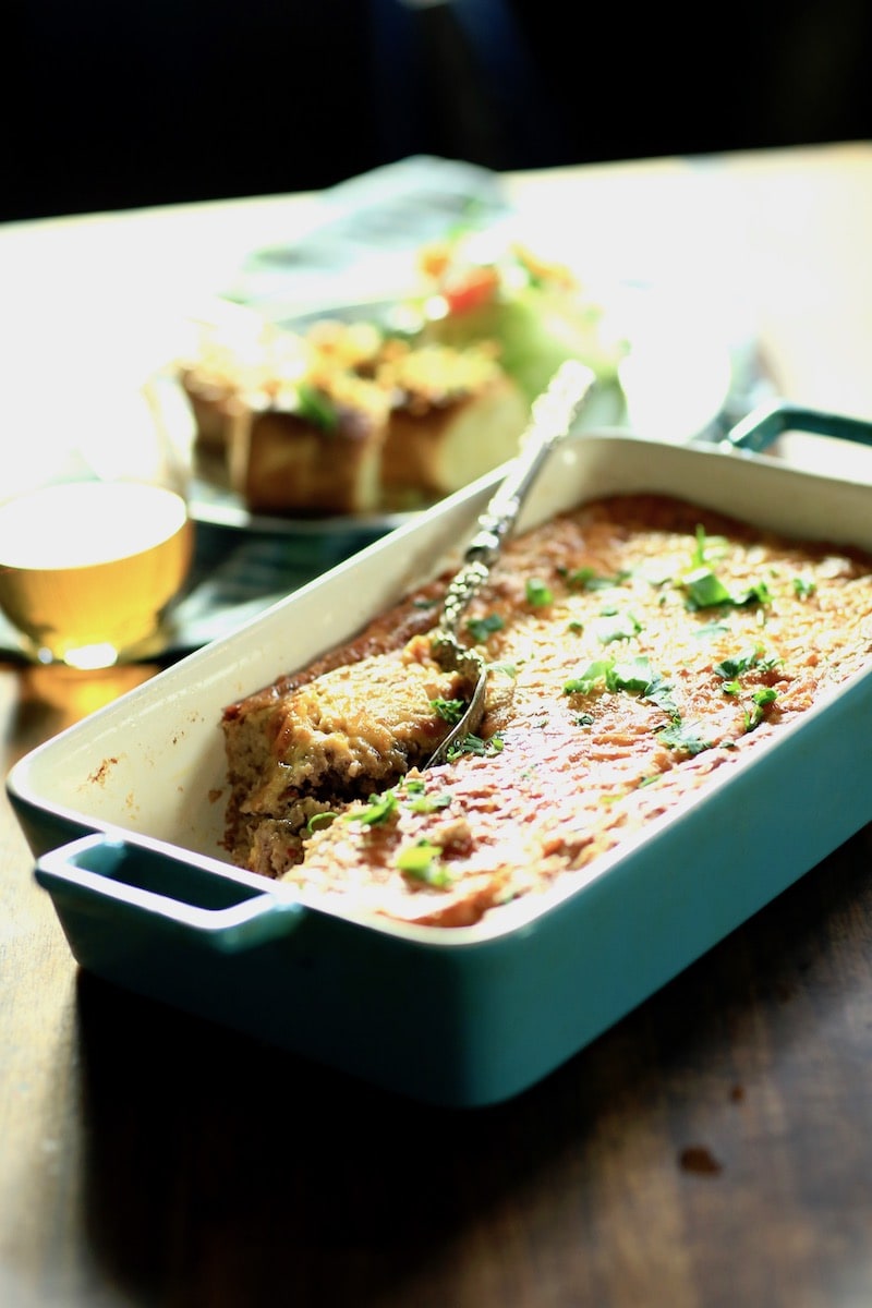 blue ceramic nonstick baking pan with baked grits casserole, spoon in pan