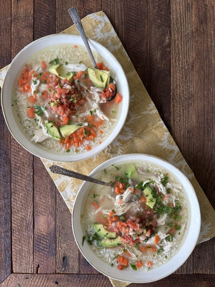 two white bowls full of Mexican chicken soup on a yellow-and-white floral cloth placemat