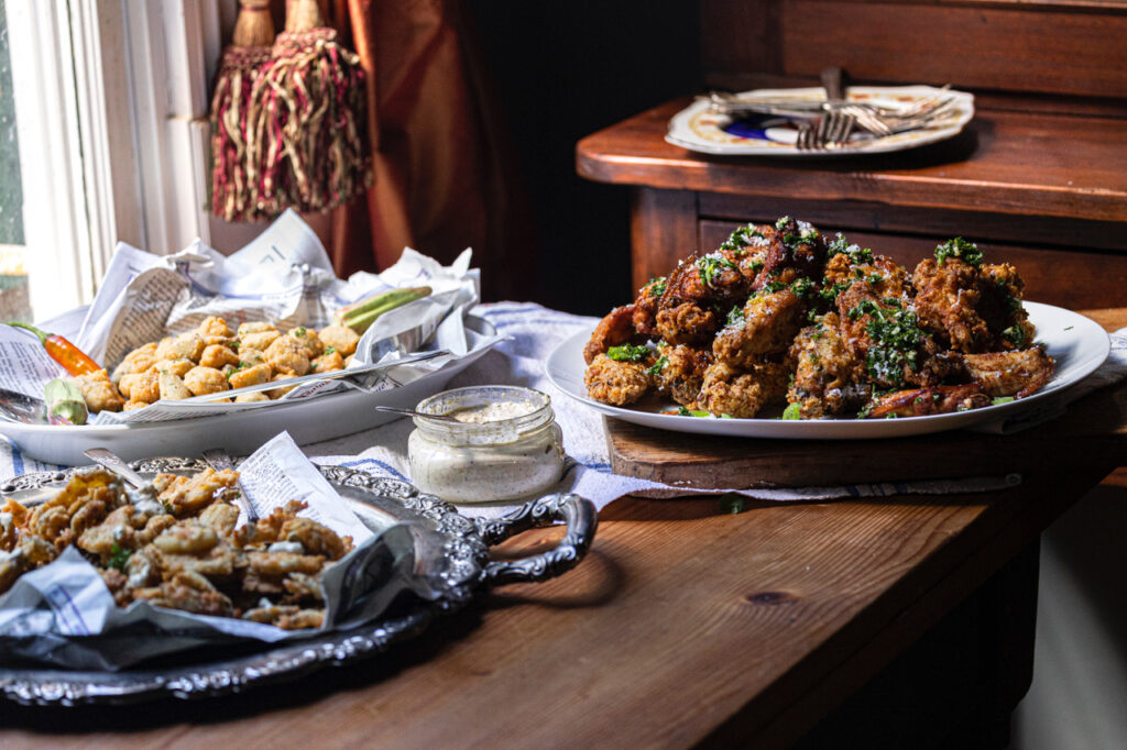 fried chicken wings heaped on a platter on wooden table along with other Super Bowl snacks