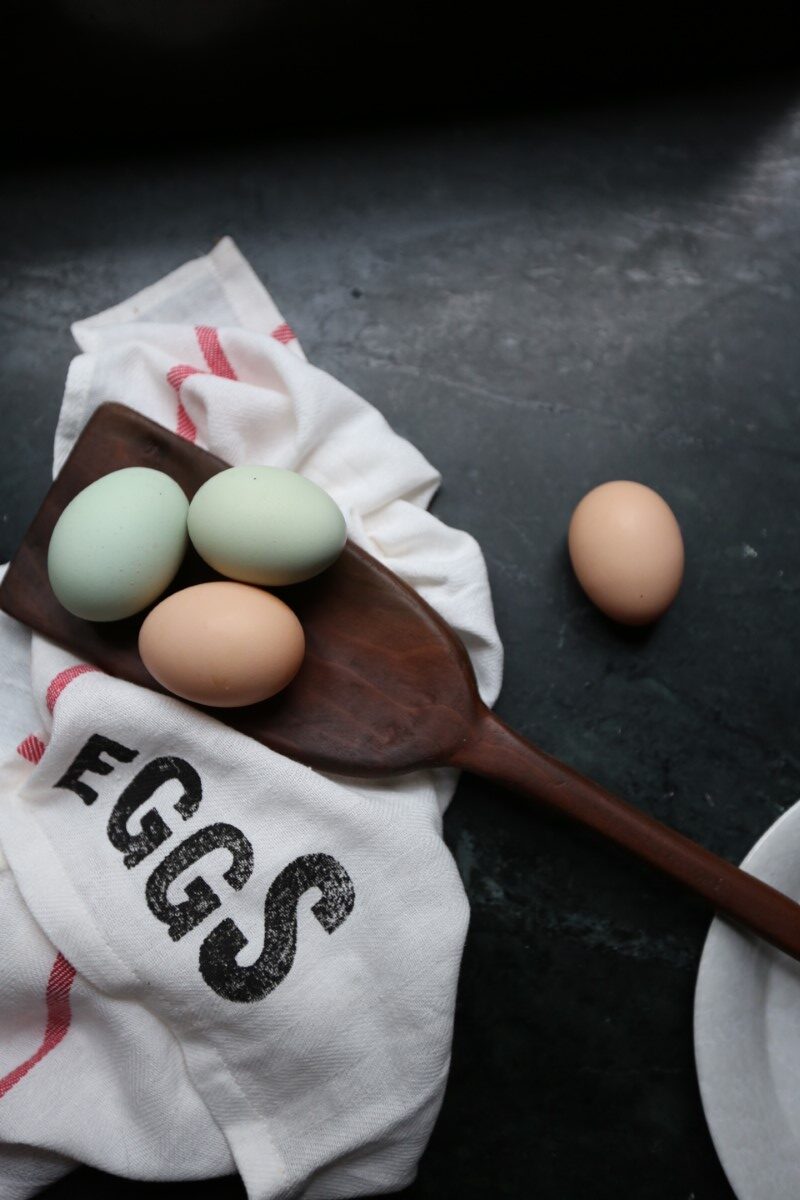 eggs on wooden spatula atop dish towel with the word EGGS