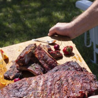 grilled BBQ ribs rack carried on cutting board outdoors