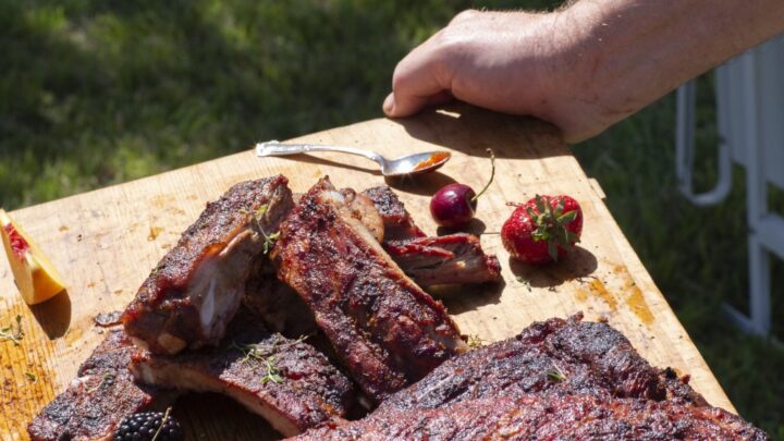 grilled BBQ ribs rack carried on cutting board outdoors