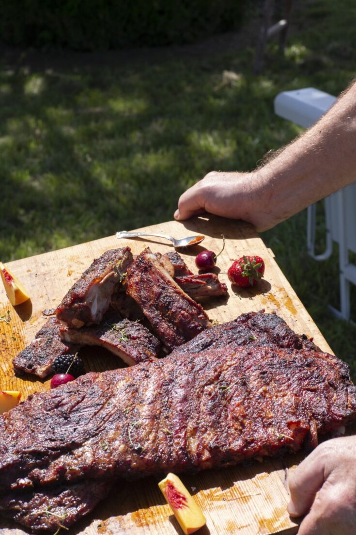 grilled BBQ ribs rack carried on cutting board outdoors