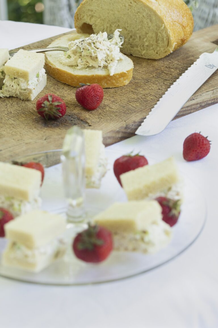 Stacy Lyn's classic chicken salad spread on slices of bread on cutting board with strawberries scattered in foreground