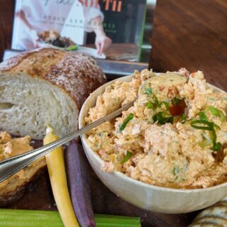 heaping bowl of pimento cheese spread on wooden cutting board with celery, bread, and crackers - Stacy Lyn's Love Language of the South cookbook in background