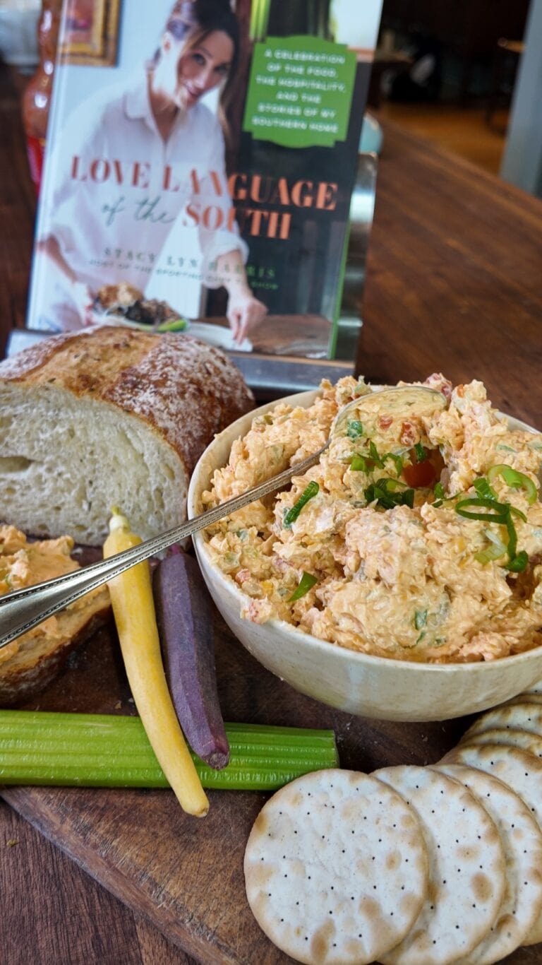 heaping bowl of pimento cheese spread on wooden cutting board with celery, bread, and crackers - Stacy Lyn's Love Language of the South cookbook in background