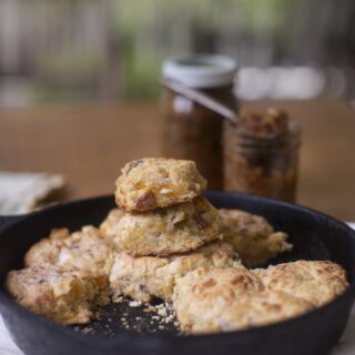 stack of fresh buttermilk cheddar biscuits in cast-iron skillet with jars of homemade jam