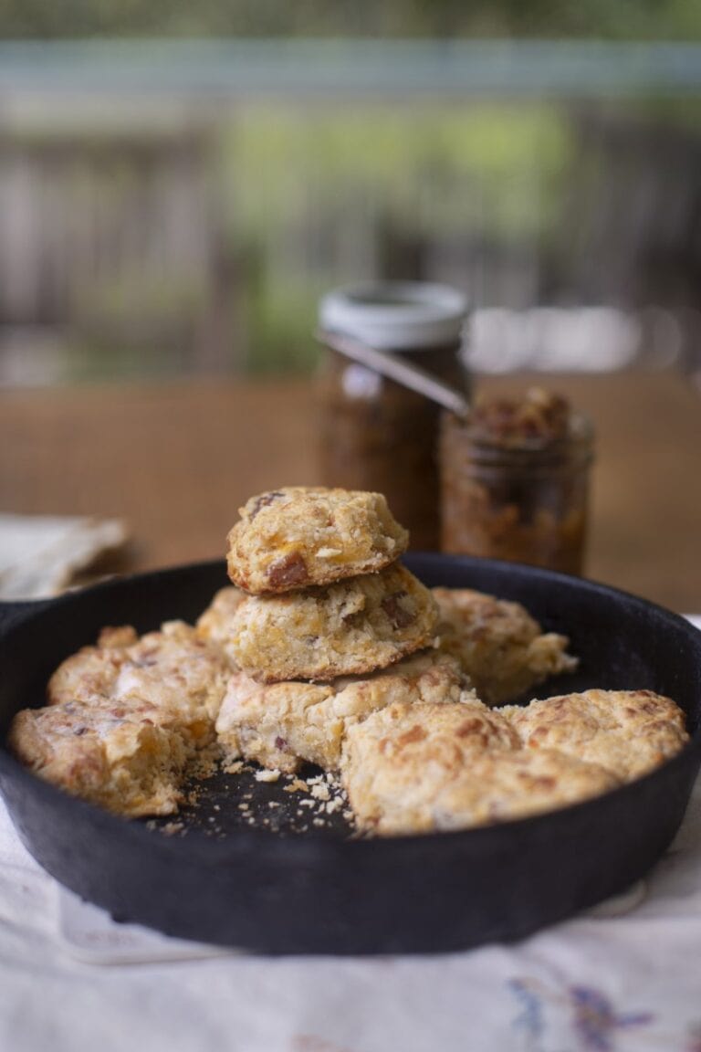 stack of fresh buttermilk cheddar biscuits in cast-iron skillet with jars of homemade jam
