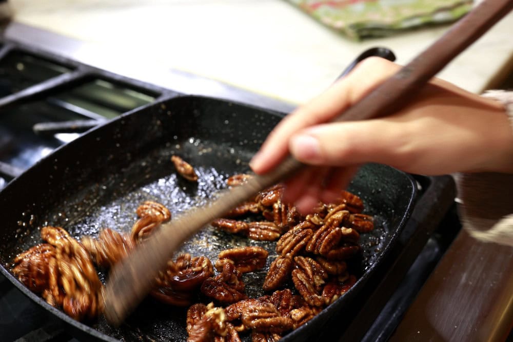 Stacy Lyn stirring candied pecans in square cast-iron skillet on stove
