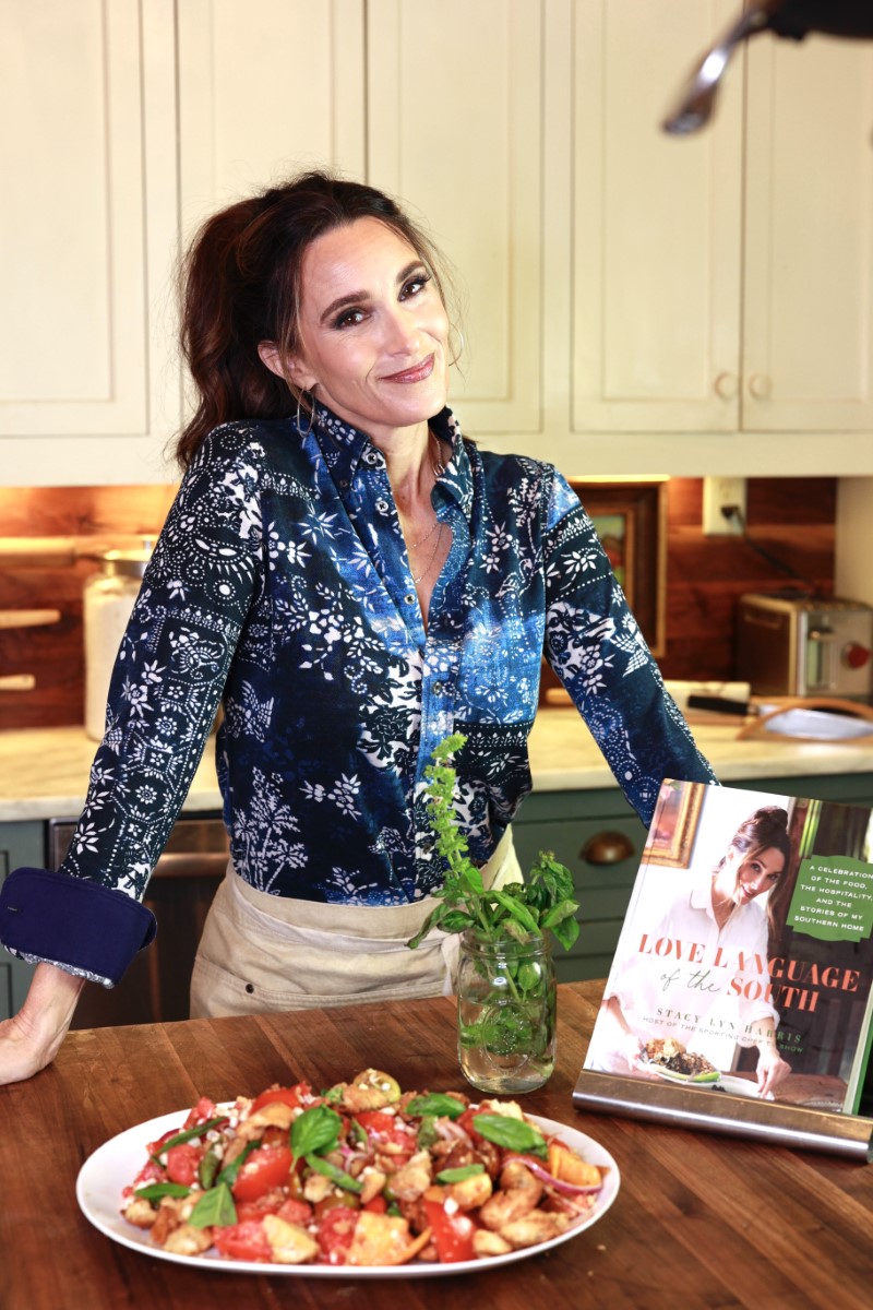 Stacy Lyn Harris smiling at kitchen counter with panzanella tomato salad and copy of her book Love Language of the South