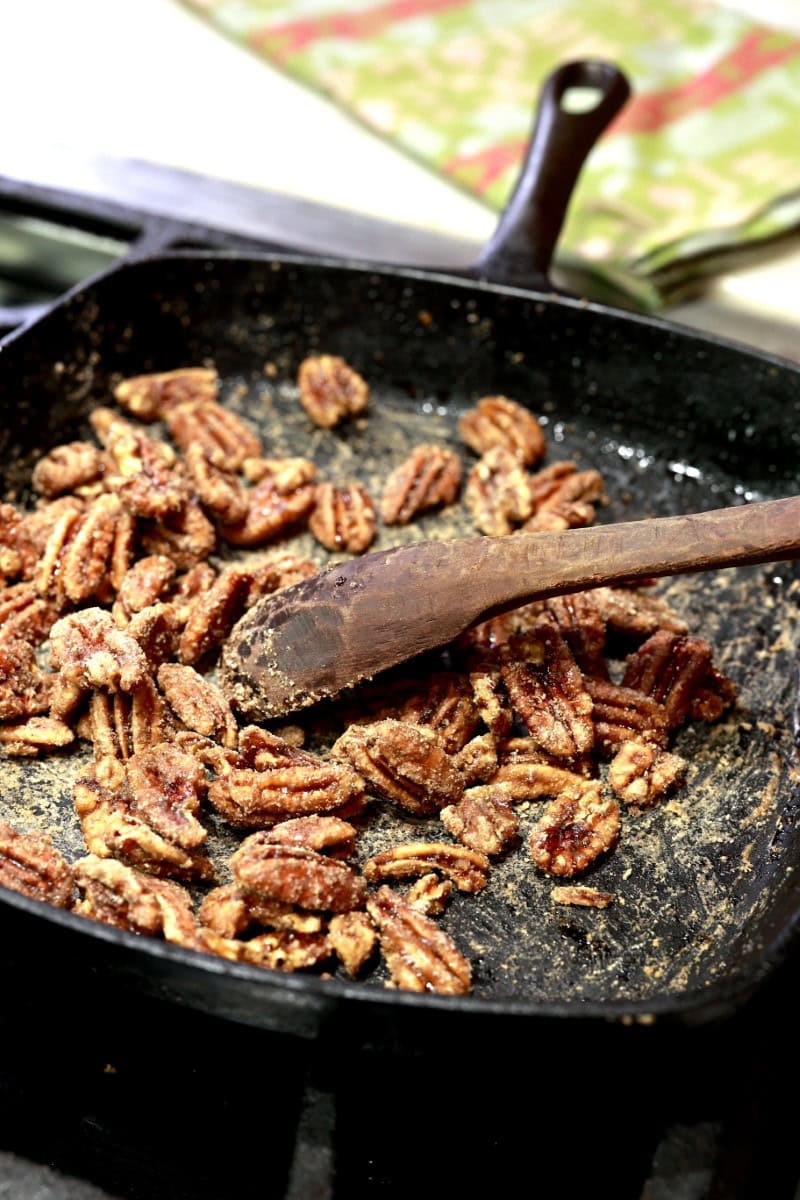 stirring candied pecans with wooden spoon in cast-iron skillet on chopping block table