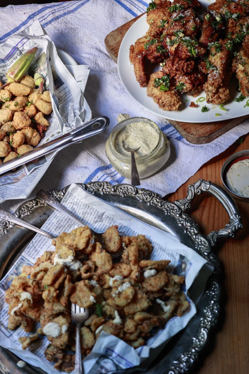 game day appetizer spread with fried pickles, chicken wings, creamy sauce, and more