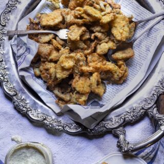 platter of golden fried pickles with fork and jar of creamy sauce on the side