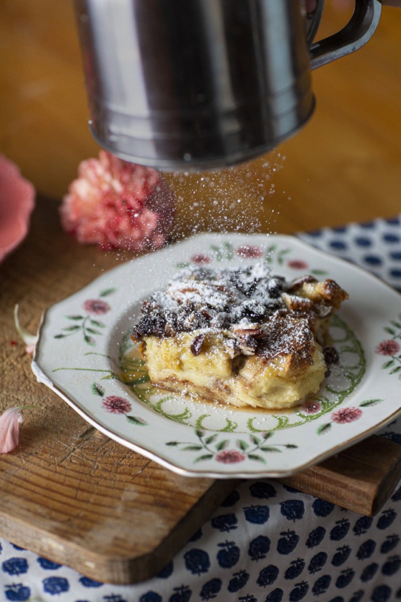 sprinkling powerdered sugar on serving of bourbon bread pudding on china floral plate