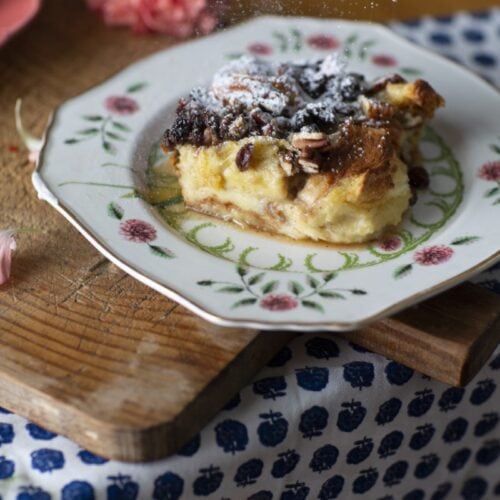 bourbon bread pudding - Stacy Lyn's bread pudding recipe served on floral china plate resting on rustic cutting board with scattered pink flowers