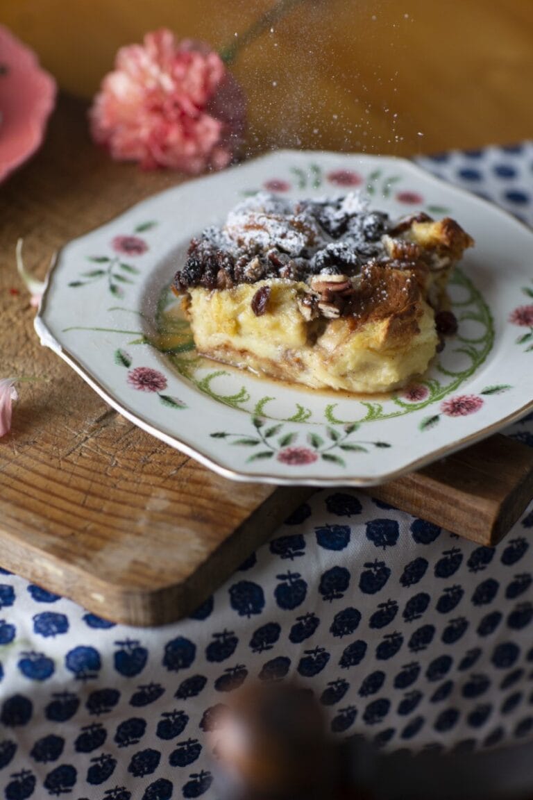 bourbon bread pudding - Stacy Lyn's bread pudding recipe served on floral china plate resting on rustic cutting board with scattered pink flowers
