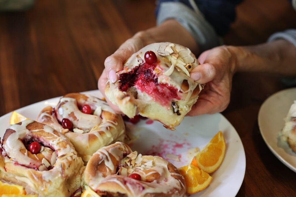 cranberry orange sticky bun lifted from platter of buns and broken apart to show bright red cranberry filling