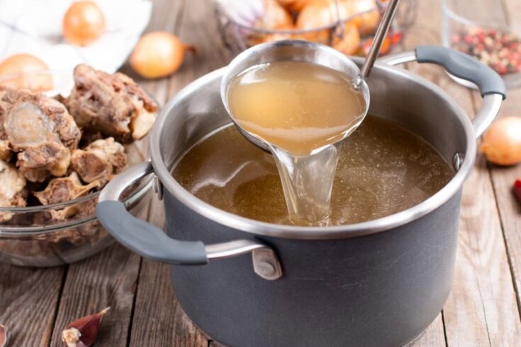 stock pot with homemade beef or venison stock, ladle lifted with spoonful, onions and bones in background