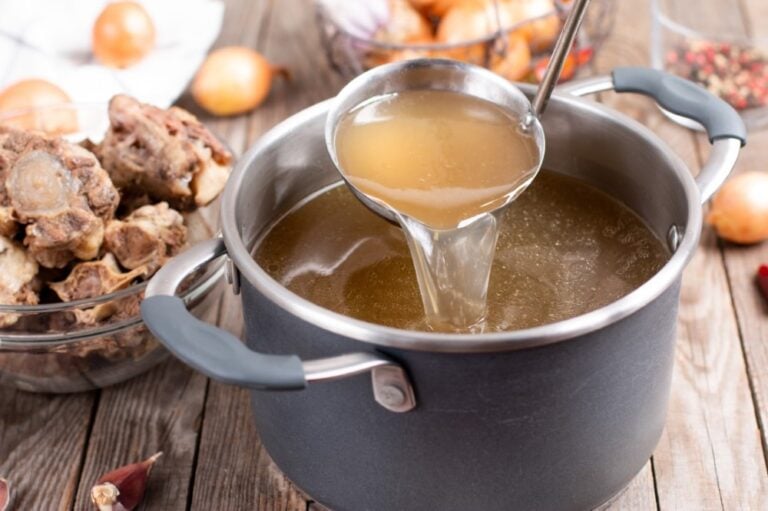 stock pot with homemade beef or venison stock, ladle lifted with spoonful, onions and bones in background