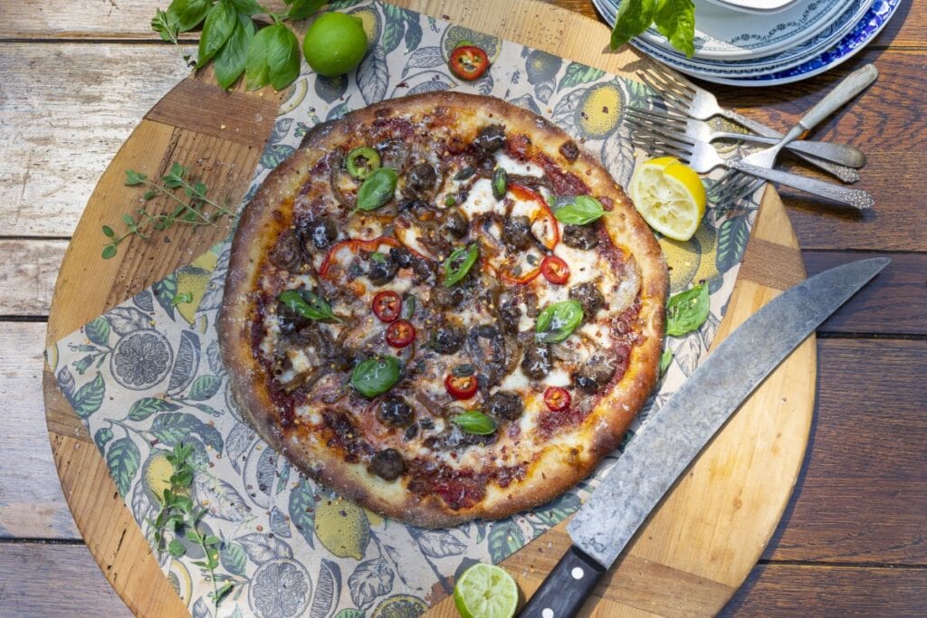 Domino's style thin crust pizza - whole homemade pizza loaded with toppings on circular cutting board with knife, forks, plates