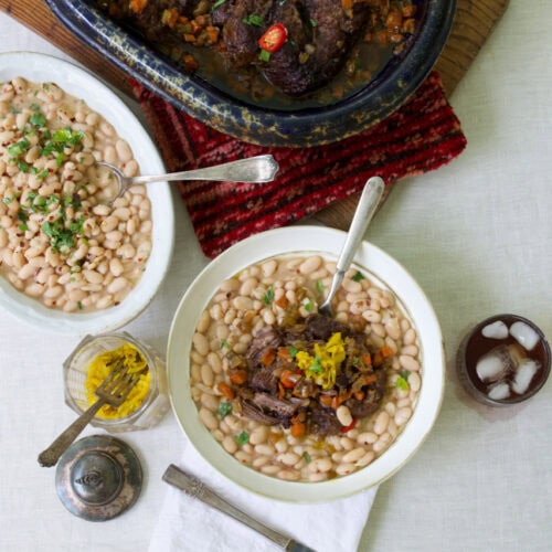 Pot Roast served in white bowl on a bed of northern beans with serving dishes of pot roast and beans in background