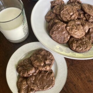 brownie cookies on a white platter and smaller white plate alongside glass of milk