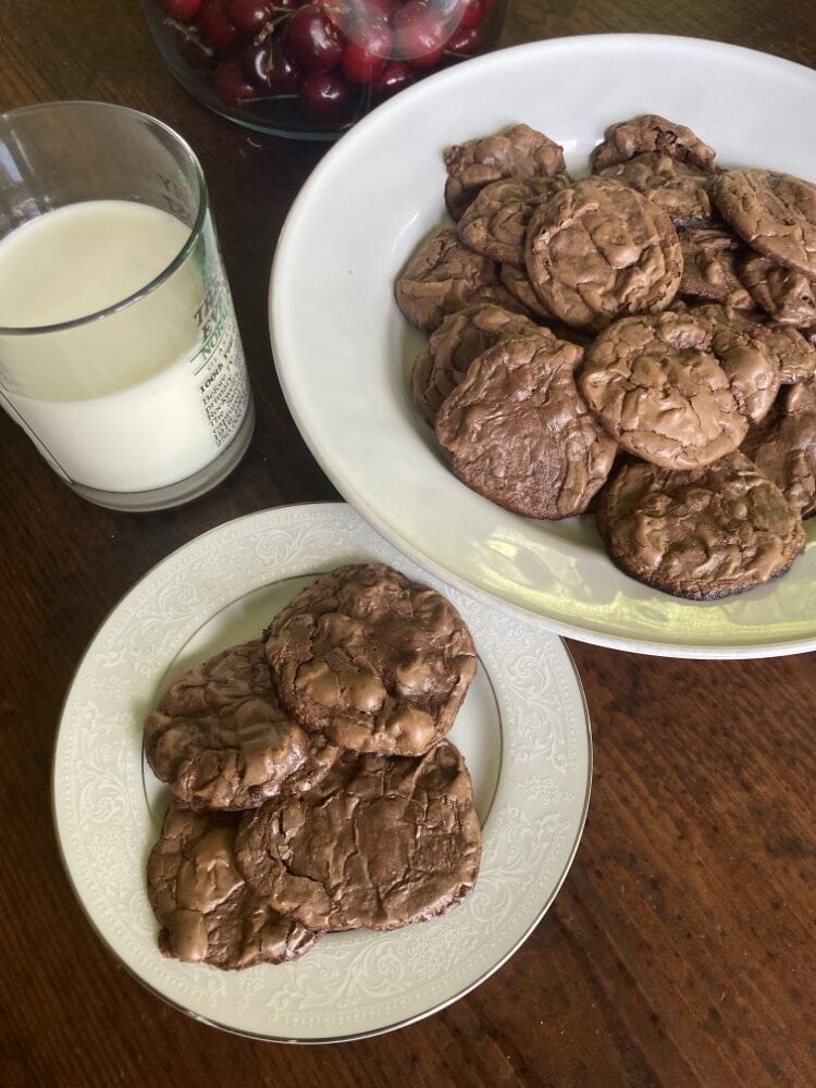brownie cookies on a white platter and smaller white plate alongside glass of milk